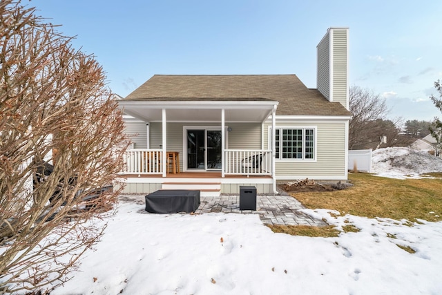 snow covered back of property with covered porch and a chimney