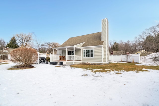 snow covered rear of property with fence, covered porch, and a chimney