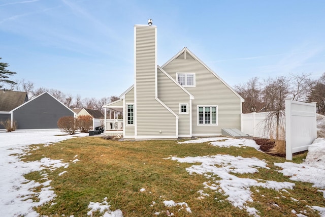 snow covered house with a lawn, a chimney, and fence