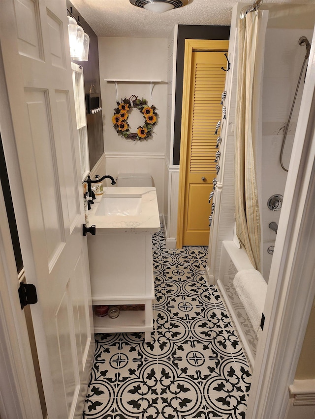 bathroom with vanity, a wainscoted wall, shower / bath combo with shower curtain, a textured ceiling, and tile patterned floors