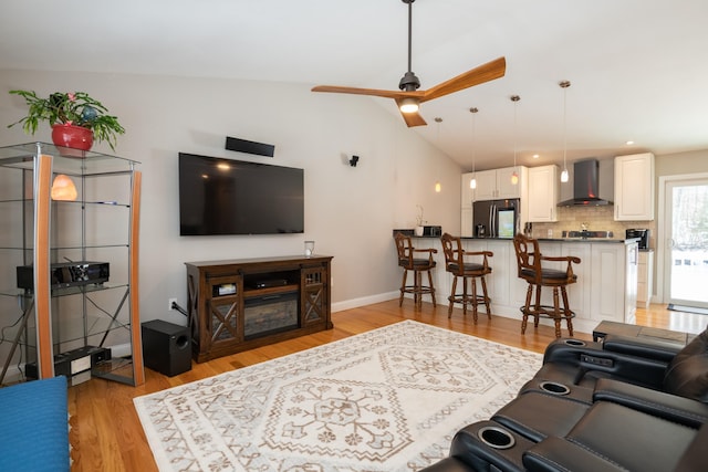 living room with lofted ceiling, light wood-style floors, baseboards, and ceiling fan