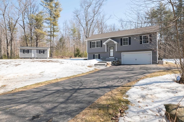 raised ranch with aphalt driveway, an outbuilding, and an attached garage