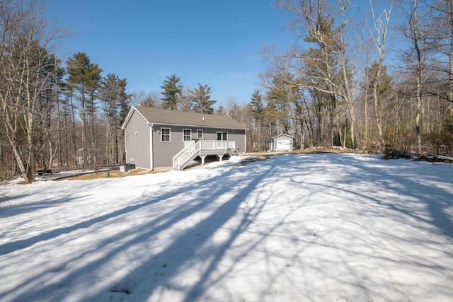 snow covered house with a deck, a storage shed, and an outdoor structure