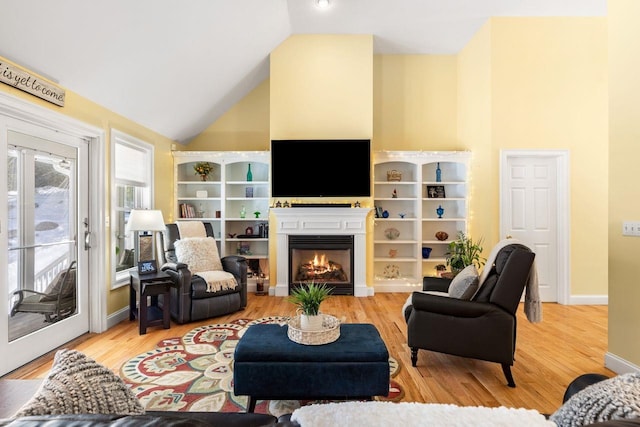 living room featuring high vaulted ceiling, a lit fireplace, and wood finished floors