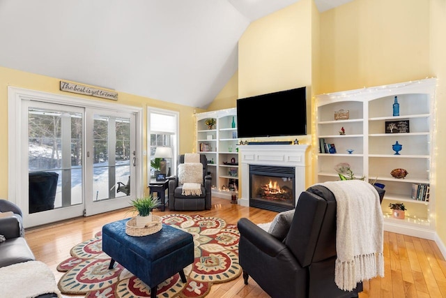 living room with wood finished floors, high vaulted ceiling, and a glass covered fireplace