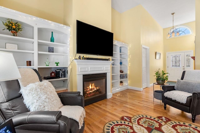 living area featuring a glass covered fireplace, a high ceiling, baseboards, and wood finished floors