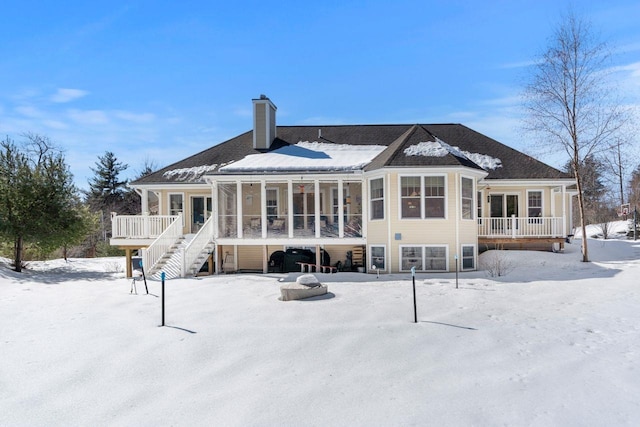 snow covered house featuring stairway, a chimney, and a sunroom