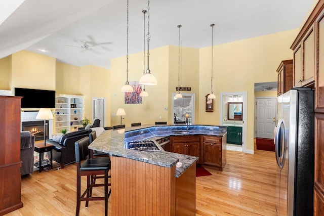 kitchen featuring a spacious island, a lit fireplace, light wood-style flooring, a kitchen breakfast bar, and stainless steel appliances