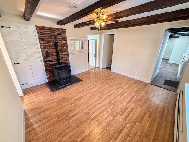 unfurnished living room with baseboards, beamed ceiling, light wood-type flooring, a wood stove, and a ceiling fan