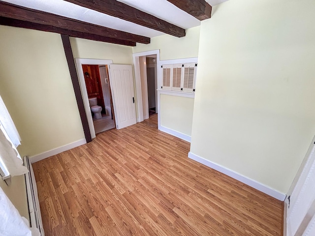 empty room featuring beam ceiling, baseboards, and light wood finished floors