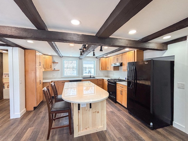 kitchen with dark wood-type flooring, black appliances, light brown cabinets, under cabinet range hood, and light countertops