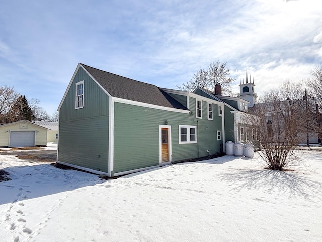 snow covered rear of property featuring a detached garage and an outbuilding