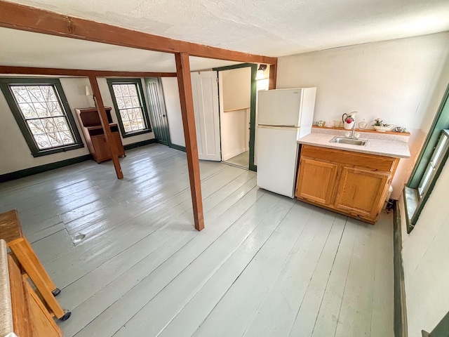 kitchen with light countertops, light wood-style flooring, freestanding refrigerator, and a sink