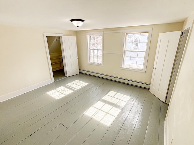 unfurnished bedroom with a baseboard heating unit, baseboards, and wood-type flooring