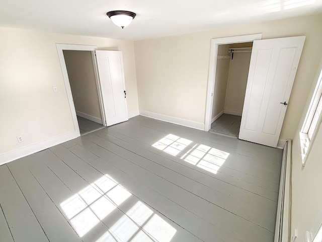 unfurnished bedroom featuring wood finished floors, baseboards, a closet, and a baseboard radiator