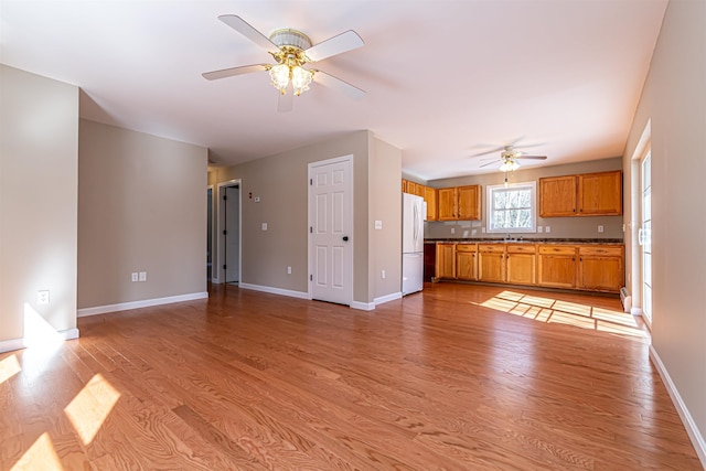 unfurnished living room with a sink, baseboards, a ceiling fan, and light wood finished floors