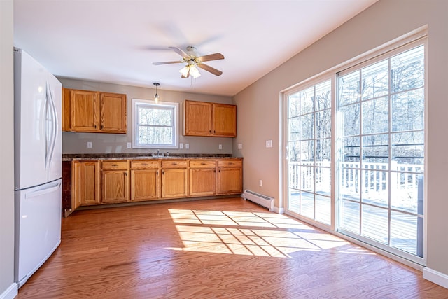 kitchen with a sink, a baseboard heating unit, freestanding refrigerator, brown cabinetry, and light wood finished floors