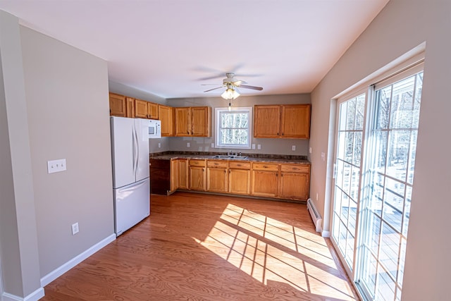 kitchen featuring white appliances, a baseboard heating unit, light wood-style floors, and a sink