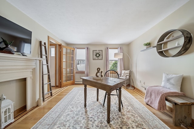 office space featuring a baseboard heating unit, baseboards, a textured ceiling, and light wood finished floors