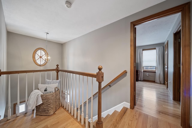 corridor featuring an upstairs landing, a notable chandelier, light wood finished floors, and baseboards