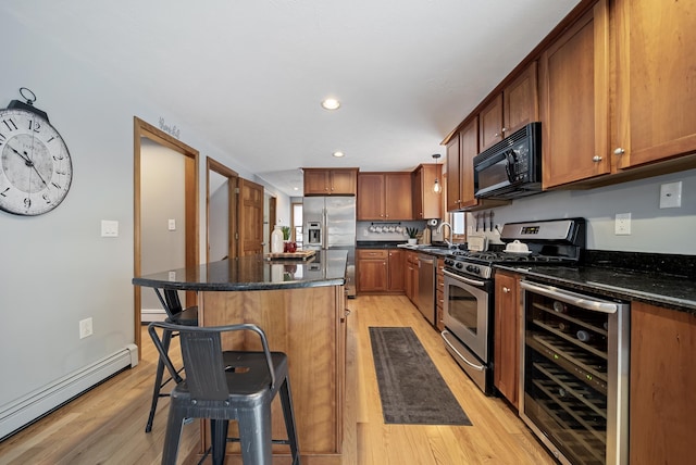 kitchen with beverage cooler, appliances with stainless steel finishes, a baseboard heating unit, light wood-type flooring, and a kitchen bar