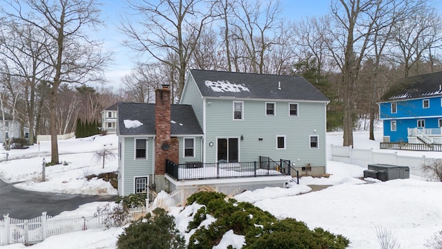 snow covered property with fence, roof with shingles, a wooden deck, a chimney, and stairs