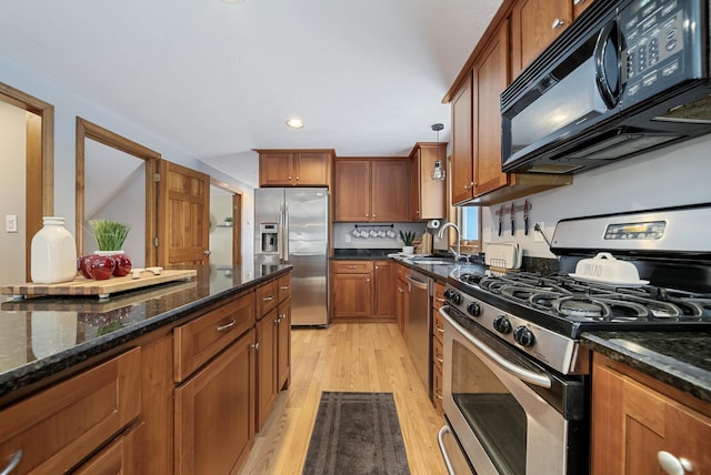 kitchen featuring dark stone counters, a sink, stainless steel appliances, light wood-style floors, and brown cabinets