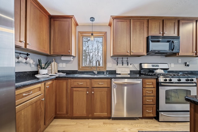 kitchen with brown cabinetry, a sink, hanging light fixtures, stainless steel appliances, and light wood-style floors