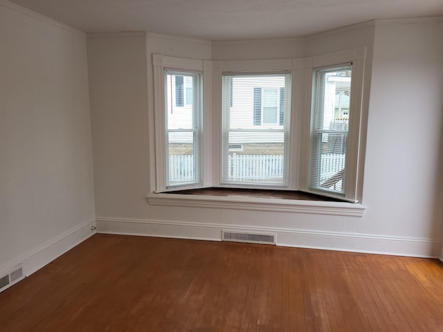 empty room featuring baseboards, wood finished floors, visible vents, and ornamental molding