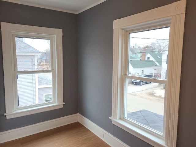 empty room featuring a wealth of natural light, light wood-style flooring, crown molding, and baseboards