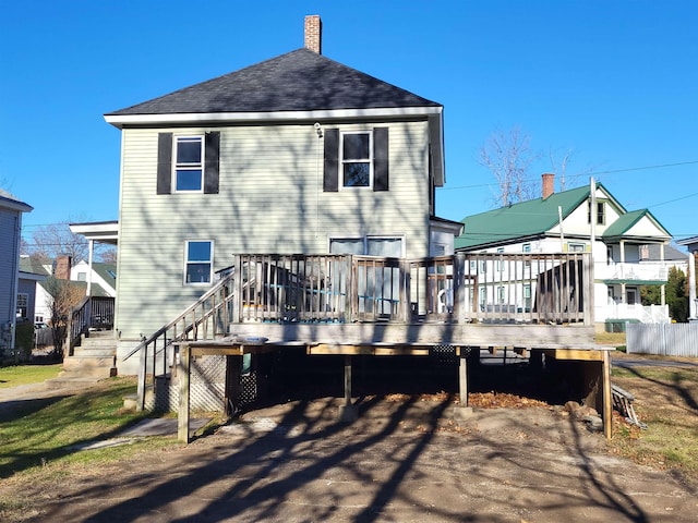 rear view of property featuring a chimney, a deck, and roof with shingles