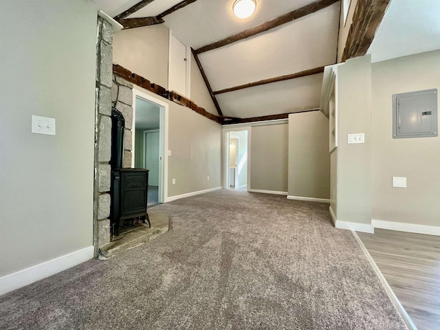 unfurnished living room with electric panel, beam ceiling, a wood stove, and baseboards