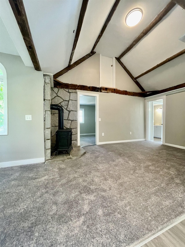 unfurnished living room with lofted ceiling with beams, a wood stove, baseboards, and carpet floors