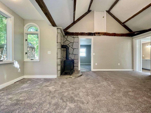 unfurnished living room featuring a wealth of natural light, carpet flooring, beam ceiling, and a wood stove