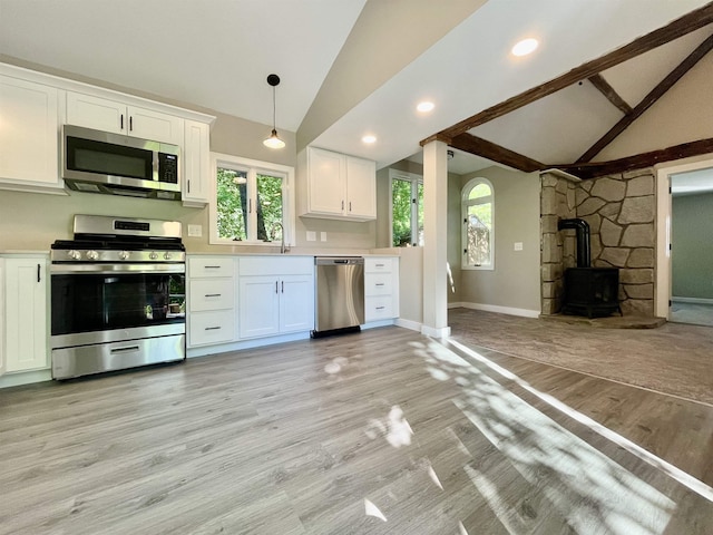 kitchen with vaulted ceiling with beams, appliances with stainless steel finishes, a wood stove, light wood-style floors, and white cabinetry