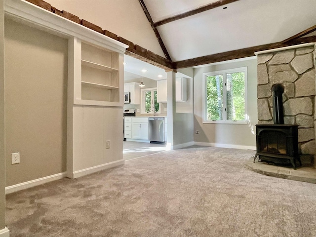 unfurnished living room with baseboards, light carpet, vaulted ceiling with beams, and a wood stove