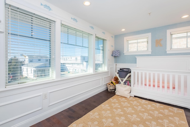 bedroom featuring a wainscoted wall, multiple windows, and wood finished floors