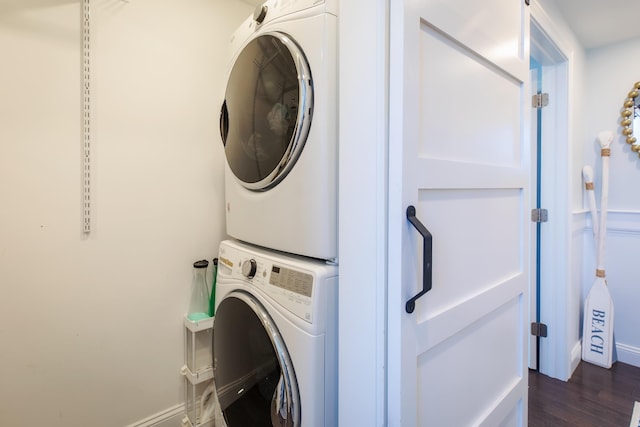 laundry area with stacked washer / dryer, laundry area, dark wood-type flooring, and baseboards