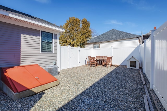 view of yard with central AC unit, a fenced backyard, and a gate