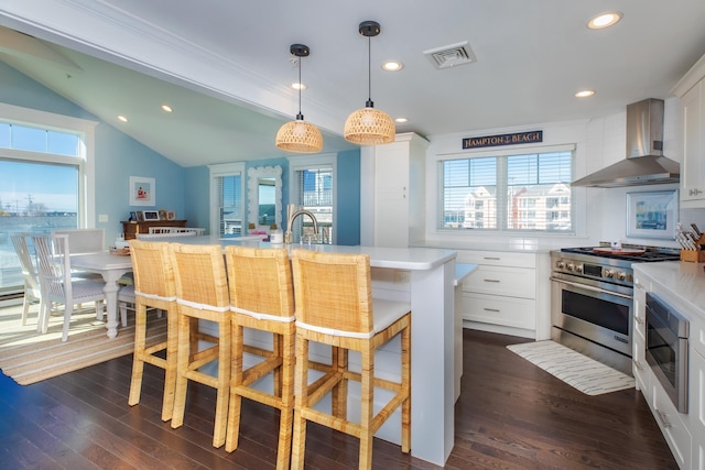 kitchen featuring visible vents, stainless steel appliances, wall chimney exhaust hood, light countertops, and lofted ceiling