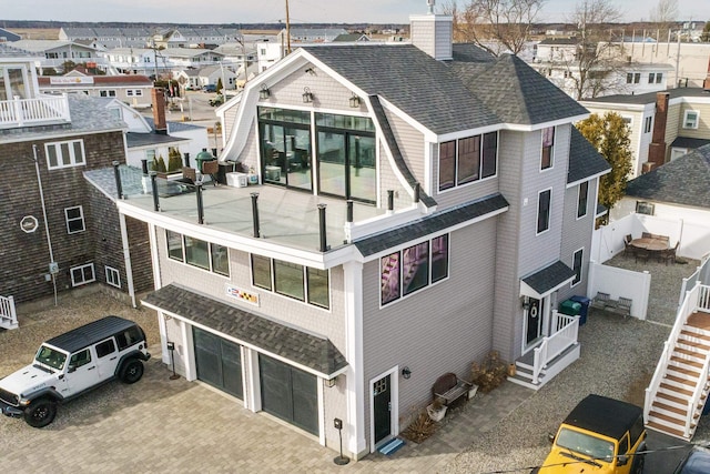 rear view of house featuring a residential view, roof with shingles, a chimney, decorative driveway, and a garage