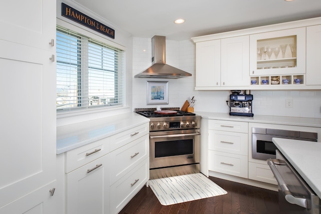 kitchen featuring tasteful backsplash, wall chimney range hood, dark wood finished floors, light countertops, and high end stainless steel range oven