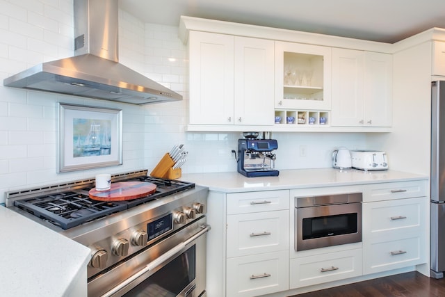 kitchen with stainless steel appliances, wall chimney exhaust hood, decorative backsplash, and light countertops