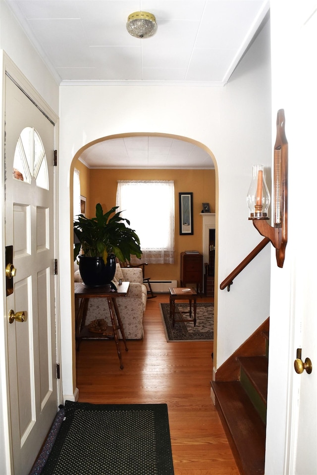 foyer entrance featuring arched walkways, ornamental molding, a baseboard radiator, and wood finished floors