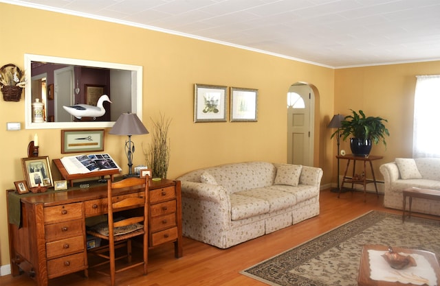 living area featuring a baseboard heating unit, arched walkways, wood finished floors, and crown molding