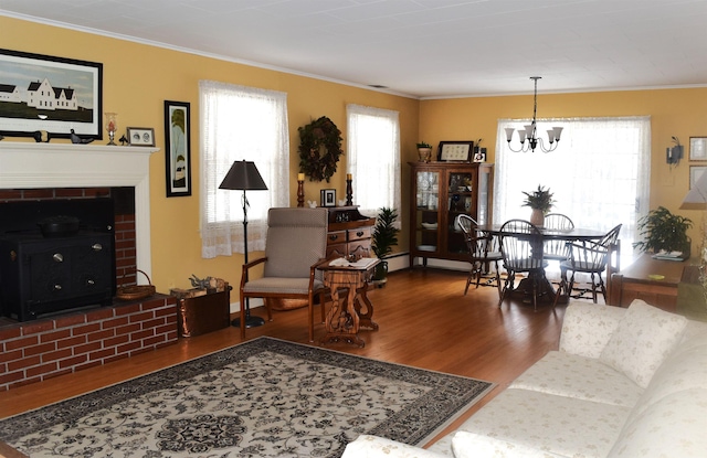 living room with ornamental molding, a baseboard heating unit, wood finished floors, a brick fireplace, and a chandelier