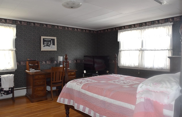 bedroom with wallpapered walls, wood finished floors, and a baseboard heating unit