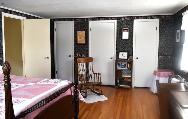 bedroom with ornamental molding, wallpapered walls, and wood finished floors