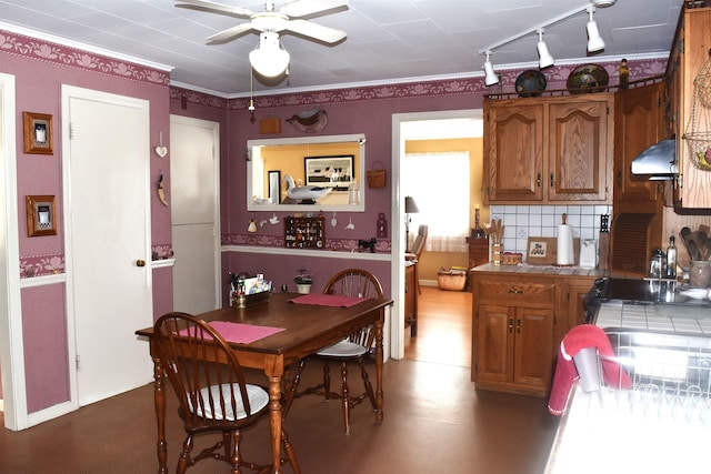 kitchen with tile countertops, a ceiling fan, brown cabinetry, wallpapered walls, and exhaust hood