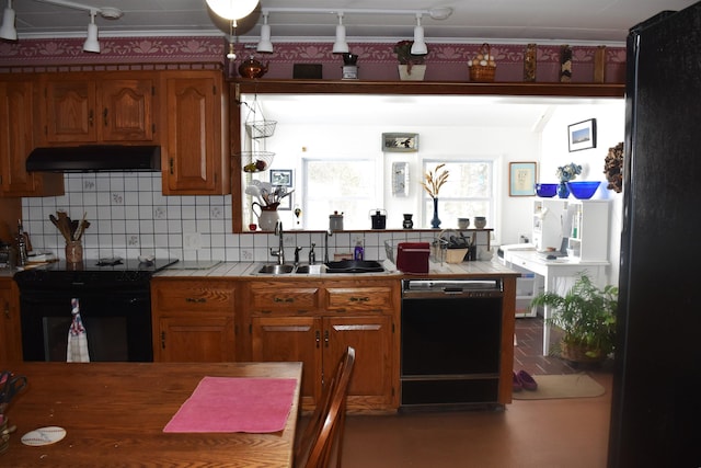 kitchen featuring tile counters, under cabinet range hood, decorative backsplash, black appliances, and a sink